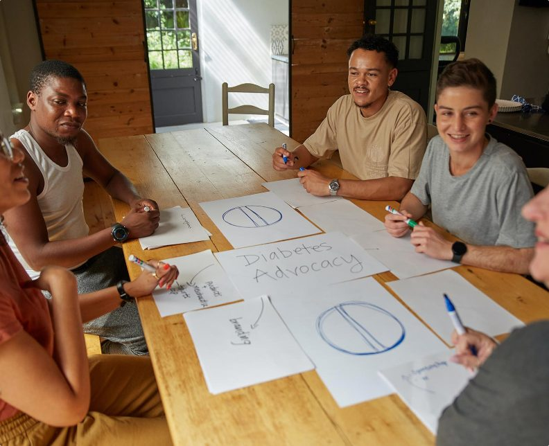 Community members collaborating around a table during a co-design workshop, sketching ideas on large sheets of paper.
